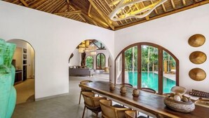 A spacious room with a large dining table, chairs, and a view of a swimming pool. - Villa La Canopee by BaliSuperHost (Bali)