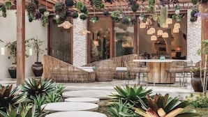 A covered outdoor seating area with wicker furniture, hanging plants, and a stone wall backdrop. - Villa La Canopee by BaliSuperHost (Bali)