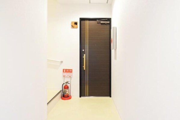 A narrow hallway with a dark wooden door, a fire extinguisher, and a small sign on the wall. - youmeiyado asahi 1F (Osaka)