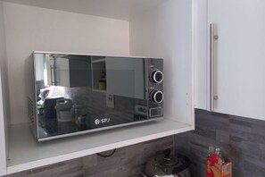 A microwave oven on a white shelf in a kitchen with a grey tiled backsplash. - Chic Modern Escape (Lusaka)