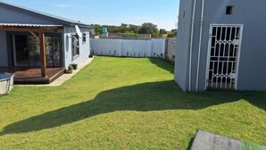 A residential backyard with a lawn, a patio area, and a white fence. - Chic Modern Escape (Lusaka)