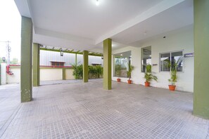 Un espace extérieur abrité, doté d’un sol carrelé, de piliers verts et de plantes en pot.