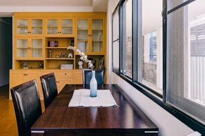 Un comedor con una mesa de madera, sillas, un florero con flores y un aparador amarillo con puertas de vidrio.