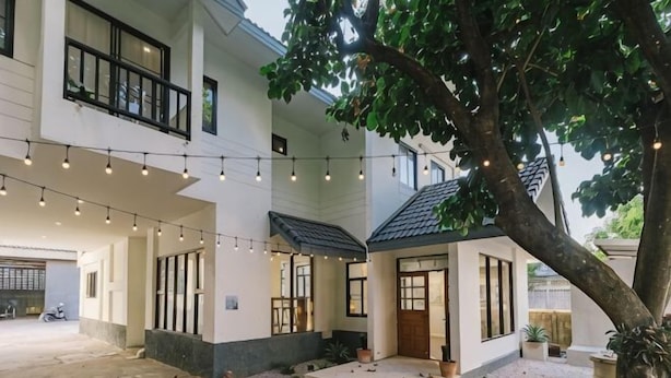 A two-story house with a covered patio, string lights, and a tree. - DEJA HOME (Chiang Mai)