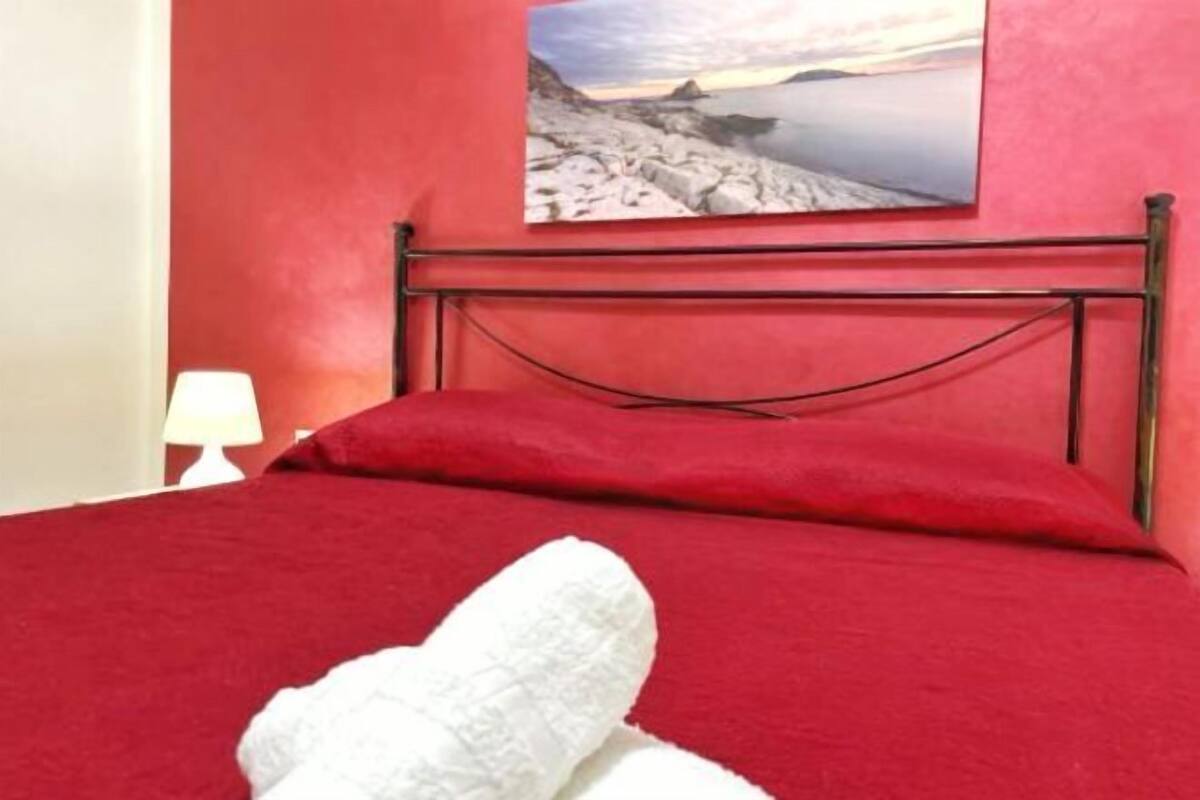 Un lit avec une couverture rouge, un oreiller blanc et une tête de lit en métal.