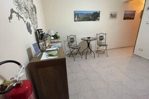 Una stanza con una reception, due sedie, un tavolino e un estintore.