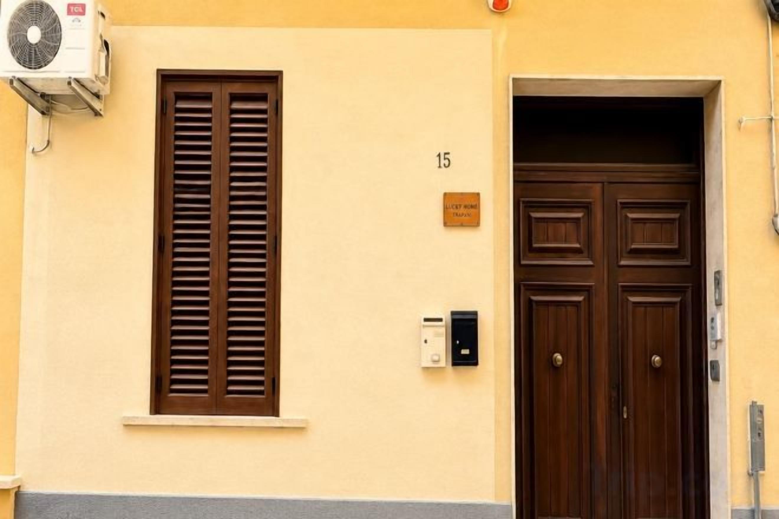 A building entrance with a double door, a window with shutters, and a number plaque.
