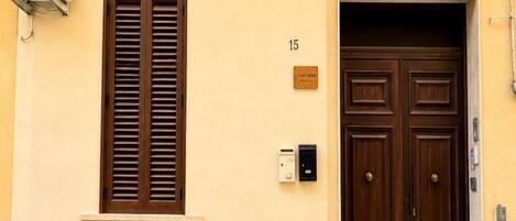 Une entrée d’immeuble avec une porte à deux battants, une fenêtre avec des volets et une plaque numérotée.