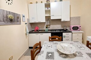 Una cucina con mobili bianchi, un forno a microonde rosa e un tavolo da pranzo con tovaglia in pizzo.