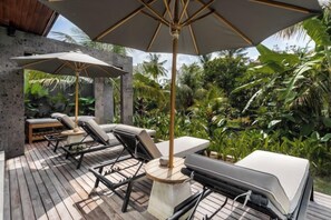 An outdoor deck with lounge chairs and umbrellas, surrounded by lush greenery. - Villa Palm Angels by BaliSuperHost (Bali)