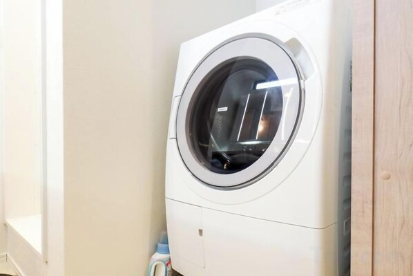 Une machine à laver à chargement frontal dans une buanderie, avec une porte en bois et un mur blanc.