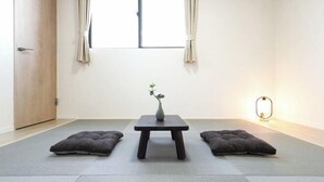 A minimalist room with tatami mats, a small table with a vase, and two cushions.