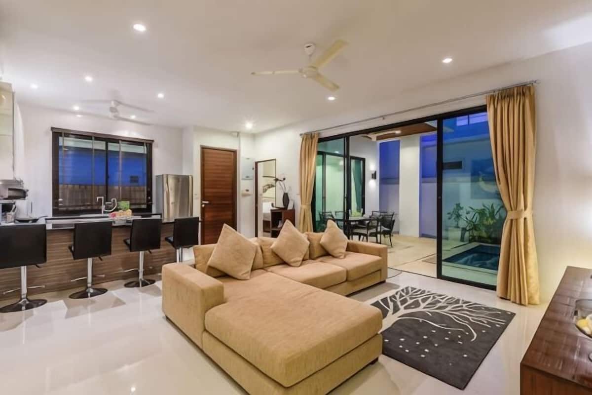 A modern living room with a sofa, a dining area, a kitchen, and a sliding glass door to a balcony.
