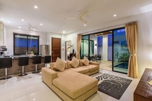 Een moderne woonkamer met een bank, een eethoek, een keuken en een schuifpui naar een balkon.