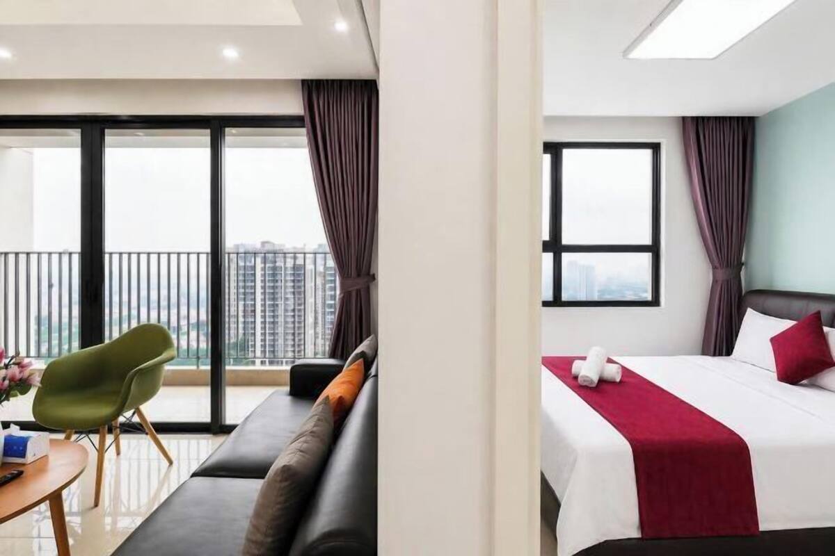 Ein Hotelzimmer mit Bett, Sofa, Tisch mit Stuhl und einem Balkon mit Blick auf Gebäude.