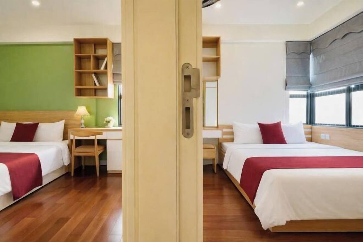 Ein Hotelzimmer mit zwei Betten, einem Schreibtisch, einem Stuhl, einem Bücherregal und einem großen Fenster.