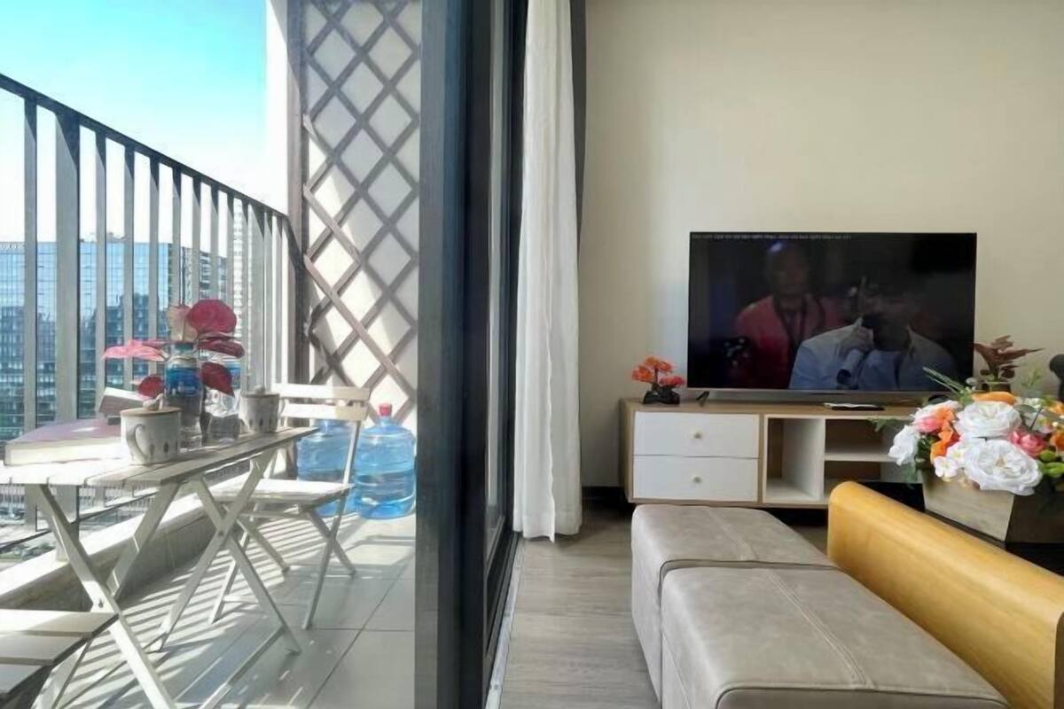 Ein Balkon mit Tisch, Stühlen, einer Couch, einem Fernseher und Blumenarrangements.