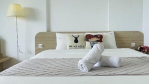 Un lit bien fait, avec une serviette enroulée, une lampe et deux coussins décoratifs ornés de motifs animaliers.