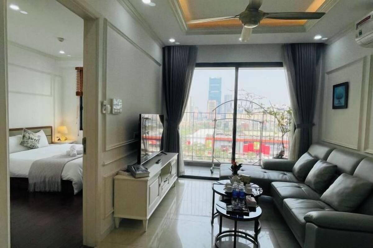 Ein Hotelzimmer mit Bett, einer Couch, einem Fernseher, einem Couchtisch und einem großen Fenster mit Blick auf die Stadt.