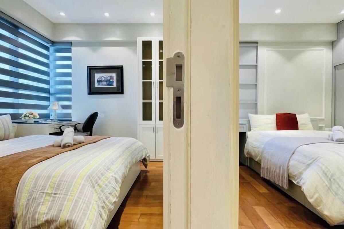 Ein Hotelzimmer mit zwei Betten, einem Schreibtisch, einem Stuhl, einem Kleiderschrank und einem gerahmten Bild an der Wand.