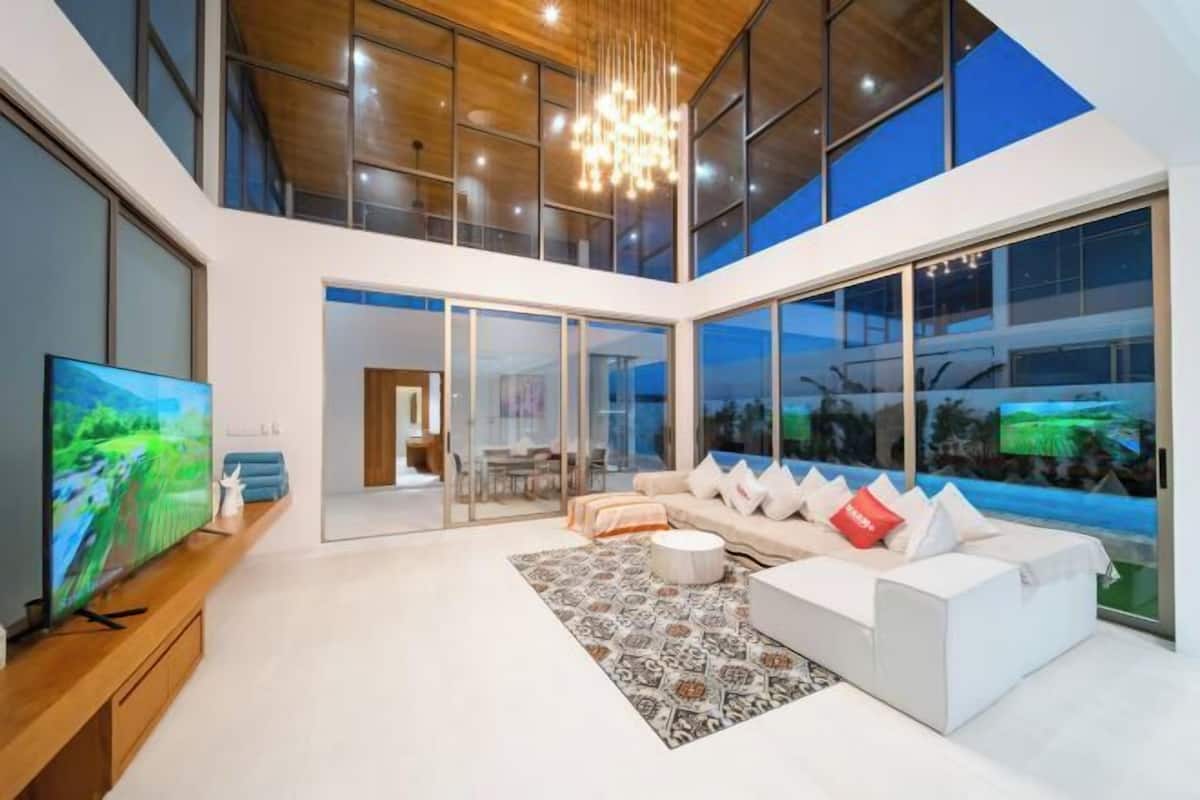 A modern living room with a large TV, a sofa set, and a chandelier.