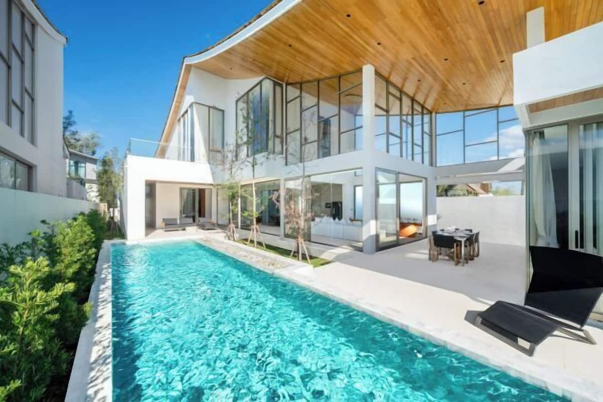 A modern house with a swimming pool, large windows, and a wooden ceiling.