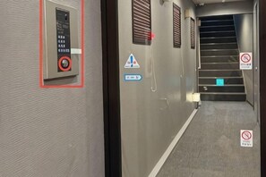 A hotel corridor with a control panel, warning signs, and a staircase. - Yasen (Kyoto)
