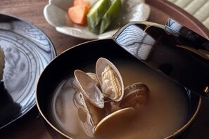 En skål suppe med muslinger, en ske og en tallerken med grøntsager.