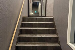 Un escalier à marches sombres menant vers le haut, avec une main courante sur le côté gauche et une fenêtre sur le côté droit.