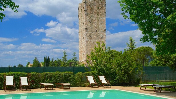 Ein Swimmingpool mit Liegestühlen und einem dahinterliegenden Steinturm.