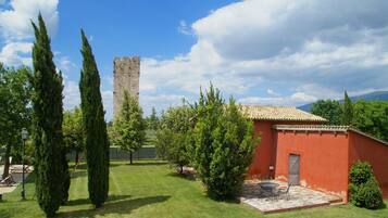 A courtyard with a red building, a tall tower, and cypress trees.