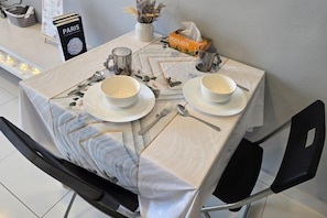 Une table dressée avec de l’assiette, des bols et des couverts blancs, un présentoir à menus portant l’inscription « PARIS » et un article de la marque « PREMIER » posé sur la table.