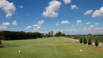 Un campo de golf con cielo despejado, árboles y una ciudad lejana.