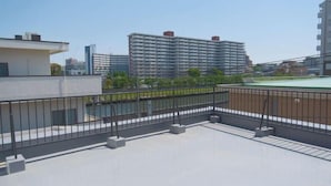 A rooftop terrace with a metal railing, a flat roof, and a view of surrounding buildings. - sakuranoyado (Tokyo)