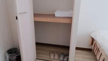 Un dormitorio con una cama, un estante de madera con toallas dobladas y un par de zapatillas en el suelo.