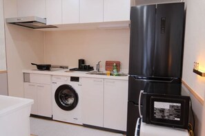 A compact kitchen with a built-in washer and dryer, a black refrigerator, and a microwave. - sakuranoyado (Tokyo)