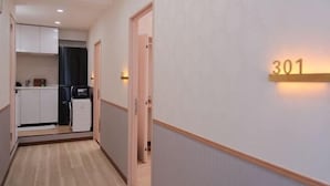 A hallway with a kitchen area, a door with a number sign, and a light fixture. - sakuranoyado (Tokyo)