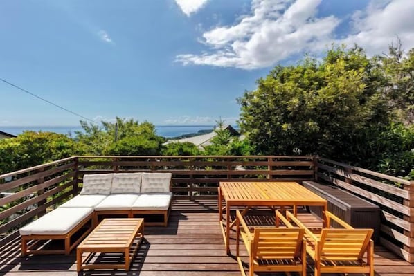 Una terraza de madera con un sofá, sillas y una mesa, con vistas a un paisaje pintoresco.