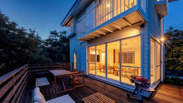 Une maison à deux étages dotée d’une terrasse, de mobilier d’extérieur et d’un barbecue.