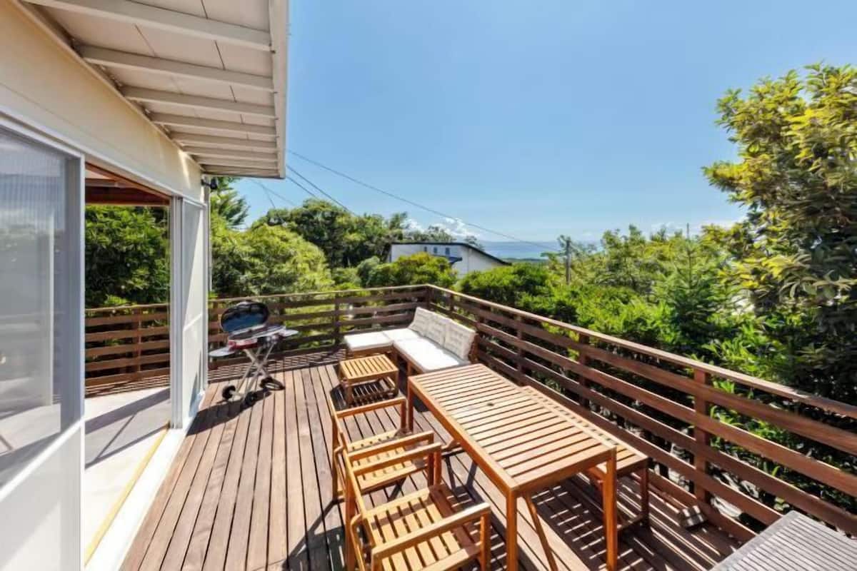 A wooden deck with outdoor furniture, a grill, and a view of the ocean.