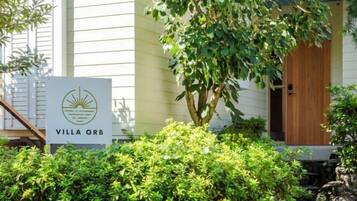 A sign for 'Villa Orb' with a logo, surrounded by greenery and a wooden door.