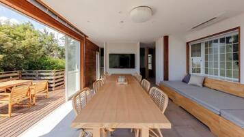 A spacious dining area with a long wooden table and chairs, a built-in bench along the wall, and large windows providing natural light.