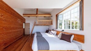 Une chambre avec un plafond en lambris de bois, un lit superposé, une grande fenêtre et un plancher en bois.