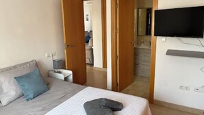 Un dormitorio con cama, televisor montado en la pared y baño a la vista a través de una puerta abierta.