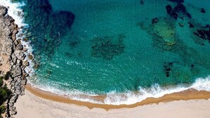 An aerial view of a beach with clear turquoise water, rocky shoreline, and a sandy beach. - Terra Hélios Suites & Studios (Trifylia)