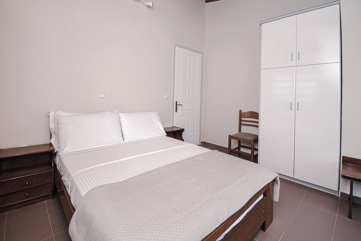 A bedroom with a bed, a nightstand, a chair, a wardrobe, and a door.