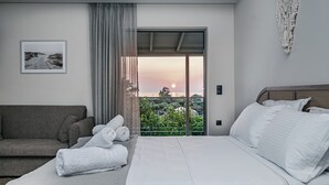 A bedroom with a bed, a sofa, and a balcony with a view of the sunset. - Terra Hélios Suites & Studios (Trifylia)