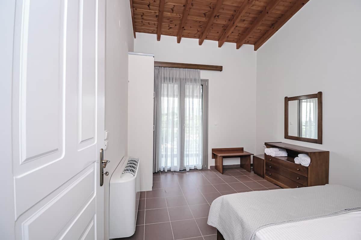 A bedroom with a bed, a wooden dresser, a mirror, a bench, and a window with curtains.