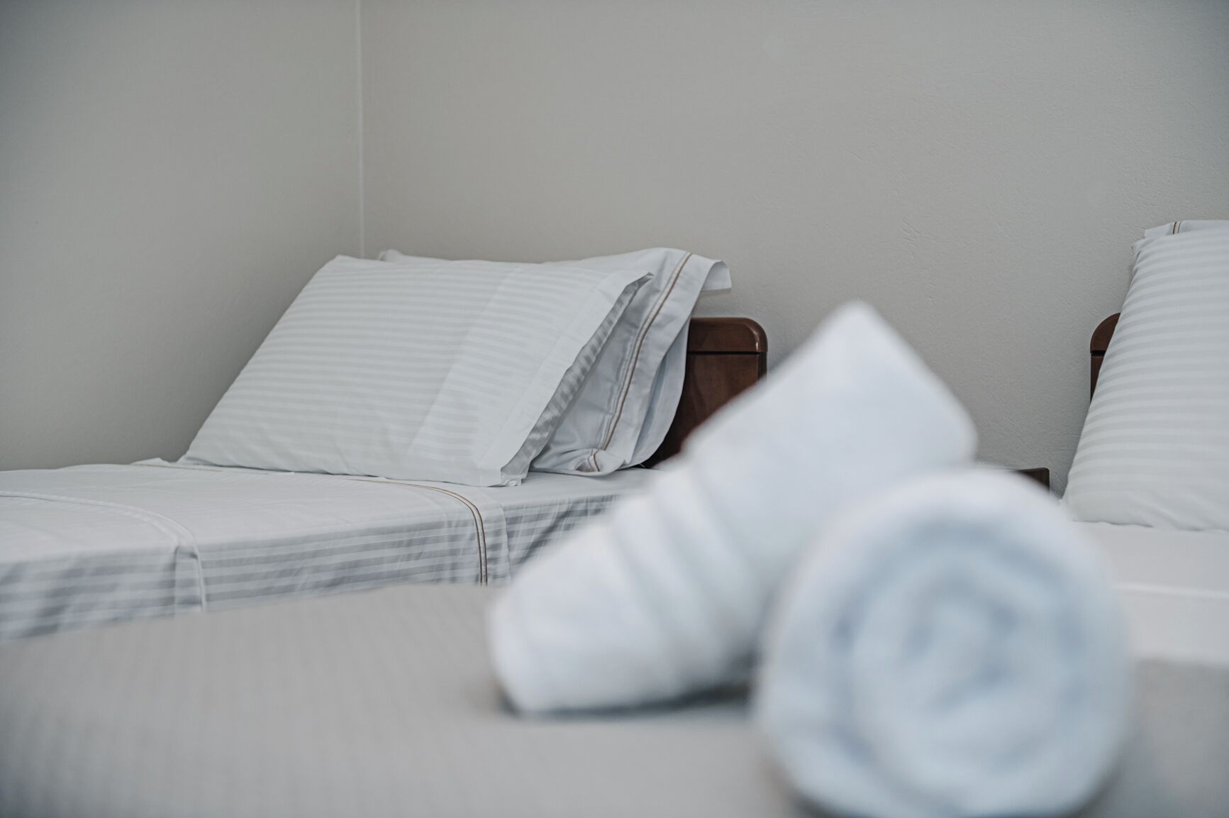 A neatly made bed with white bedding and a rolled towel on the floor.