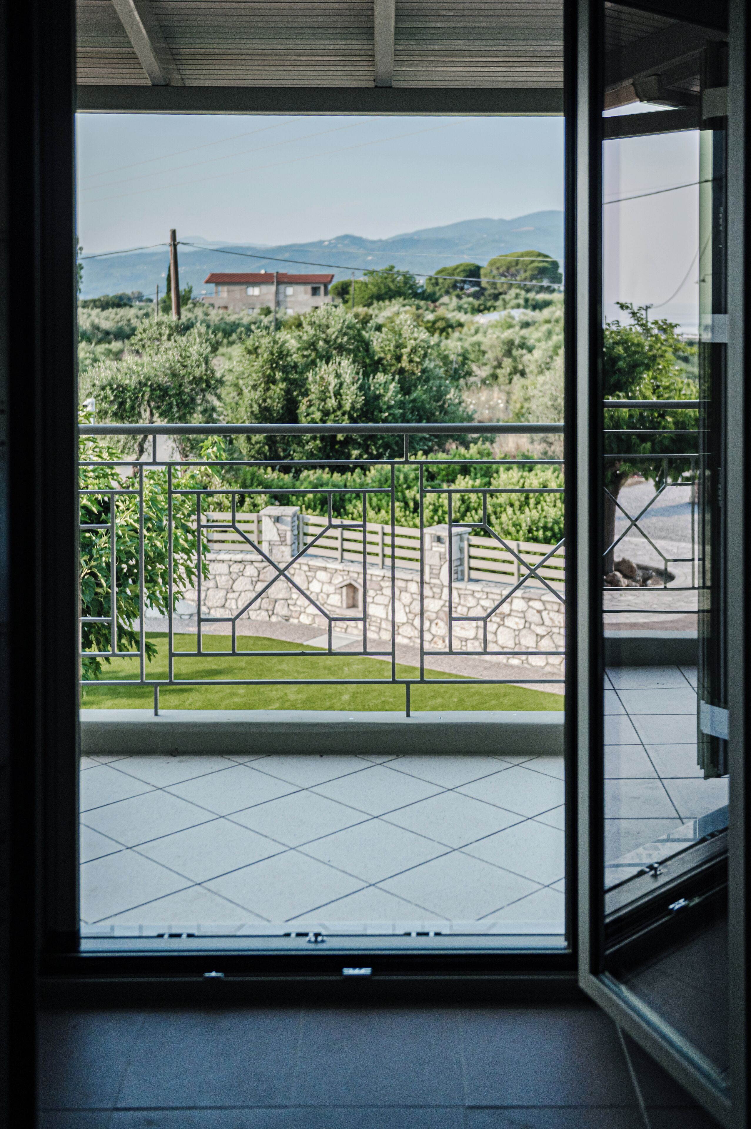 Vista desde una habitación con puerta de cristal a un espacio exterior con pared de piedra, barandilla metálica y césped.